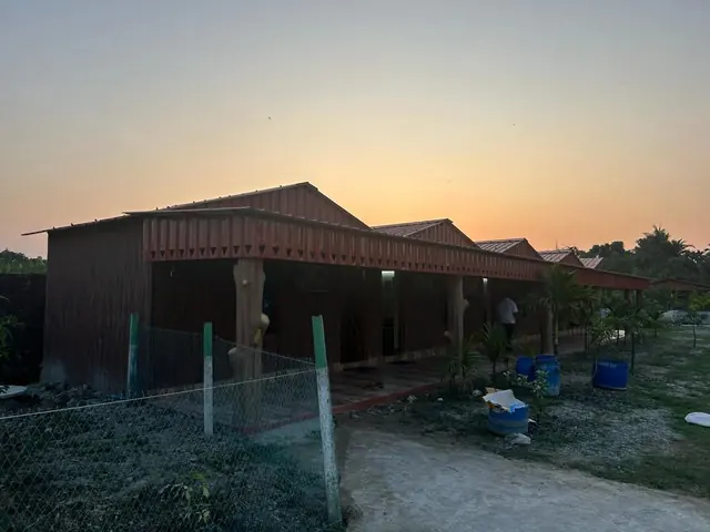 A red-roofed building with a long front veranda against an orange dusk sky