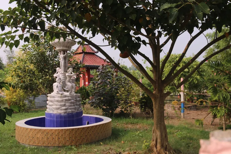 A white sculpted fountain in a blue-tiled basin beneath a spreading tree, with the red pagoda behind