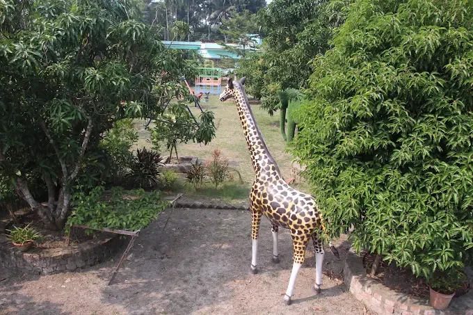 A spotted giraffe statue on a garden path between mango trees