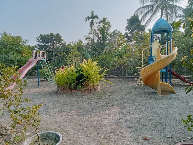 A red slide and a yellow spiral-slide play tower around a planted bed, with palm trees behind