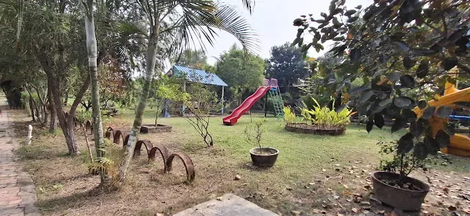 A wide view of the lawn with a red slide, a play tower and planted beds among palm trees