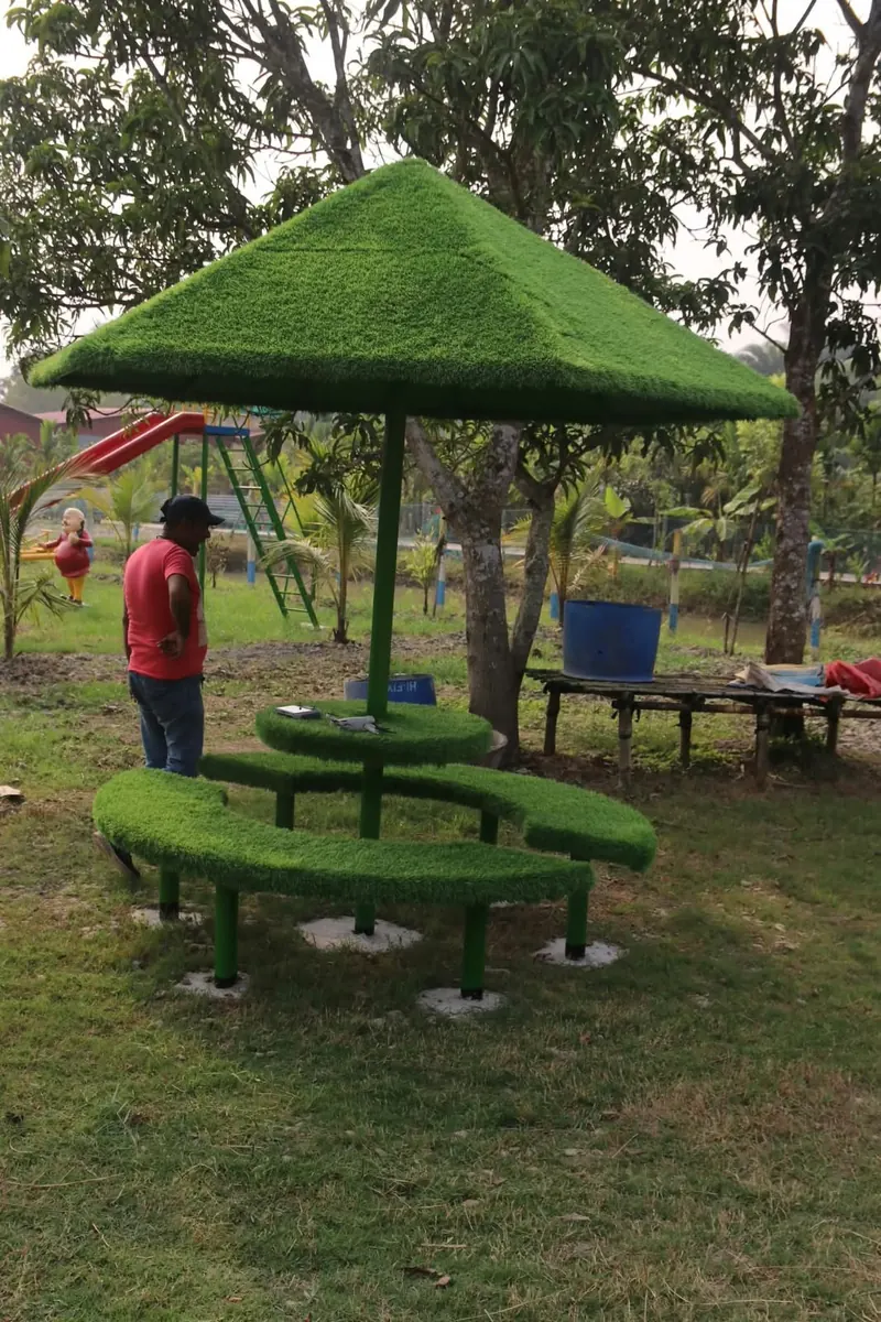 A green turf-covered umbrella table with curved benches on the lawn, with a red slide behind